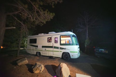 1995 Chevrolet P30 1 Ton - Step Van - A white and green RV is parked at night under trees. The RV has its interior lights on, illuminating the windows.