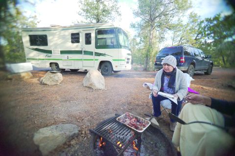 1995 Chevrolet P30 1 Ton - Step Van - A white and green 1995 Chevrolet P30 1 Ton Step Van, nicknamed "Flair 22D", is parked at a campsite next to a blue SUV. A woman sits in a c…