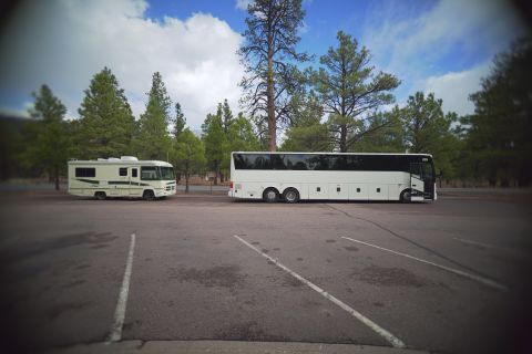 1995 Chevrolet P30 1 Ton - Step Van - A white RV and a white tour bus are parked in a lot with pine trees in the background under a partly cloudy sky.