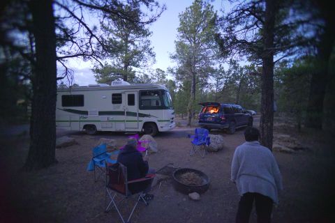 1995 Chevrolet P30 1 Ton - Step Van - A motorhome and an SUV are parked at a campsite in a wooded area. The SUV has its rear hatch open, revealing an illuminated interior.
