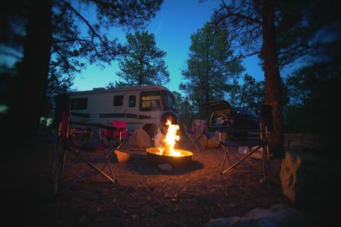 1995 Chevrolet P30 1 Ton - Step Van - A 1995 Chevrolet P30 Step Van is parked at a campsite at dusk, with a campfire burning in the foreground and a dark SUV with its trunk open…
