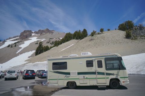 1995 Chevrolet P30 1 Ton - Step Van - Fleetwood Flair Class A motorhome parked in a lot below a snow-patched mountain ridge under blue sky.