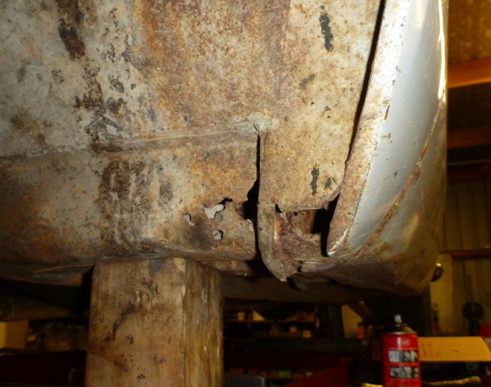 Heavily rusted metal panel with holes, supported by a wooden block.