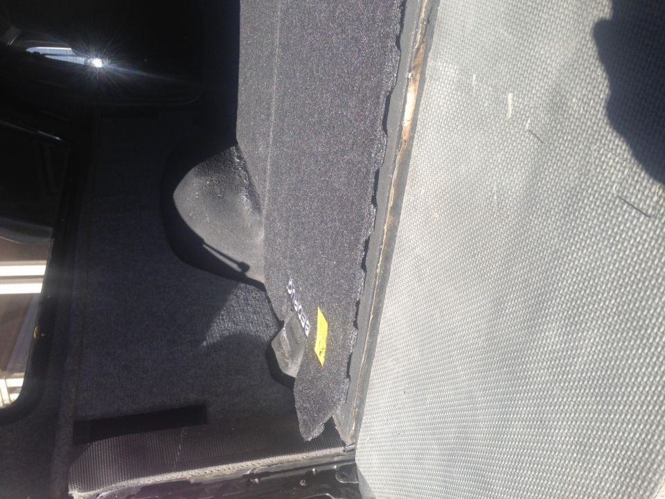 Interior cargo area of a vehicle with grey carpet and a textured mat. Yellow sticker visible.