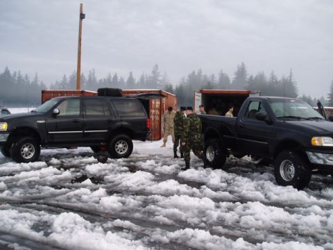1998 Ford Expedition - Two black vehicles, an SUV and a pickup truck, are parked in a snowy area with several individuals in military uniforms nearby.
