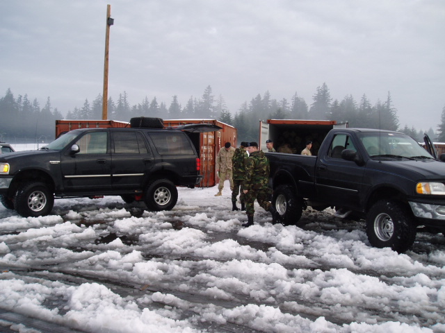 Black SUV and black pickup truck in snowy conditions with military personnel
