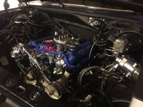 1982 Ford Bronco - The engine bay of a classic Ford truck or SUV is filled with a blue-accented V8 engine featuring chrome components and blue spark plug wire…