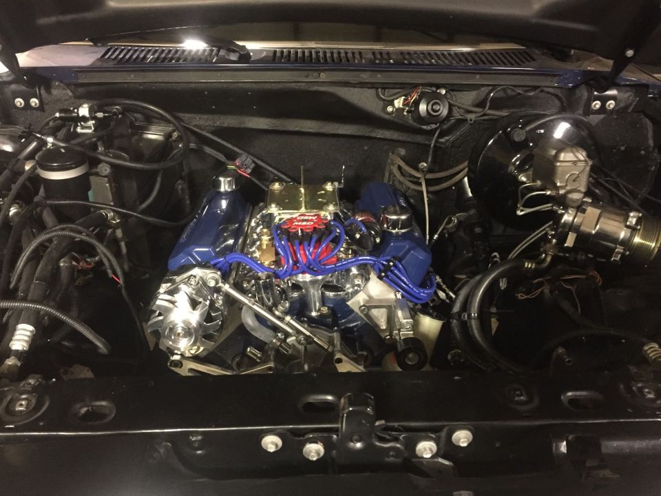 Modified V8 engine with chrome and blue accents in an engine bay.