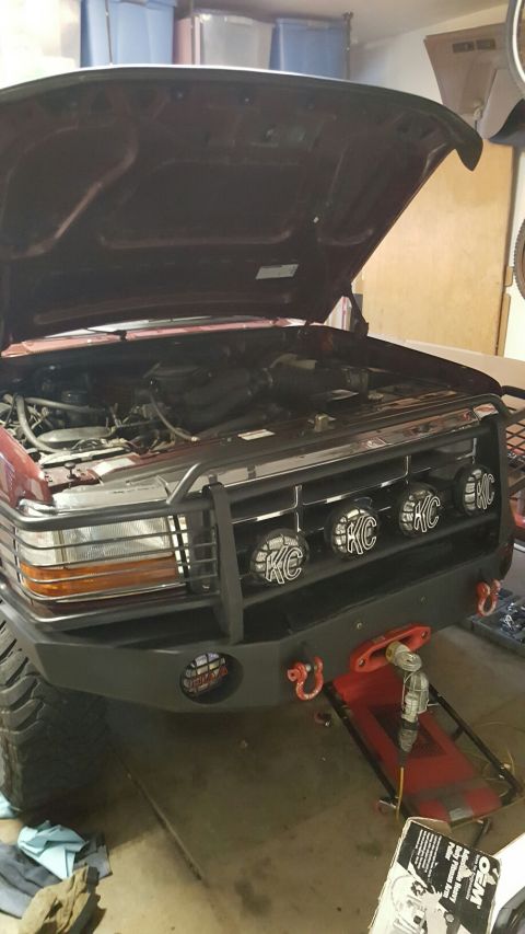 1996 Ford Bronco - The front end of a red Ford Bronco is shown with the hood open, revealing the engine bay. The vehicle has a custom aftermarket bumper with…