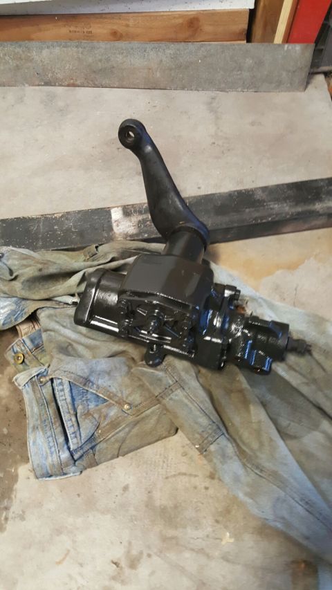 1996 Ford Bronco - A black steering gear box assembly with a pitman arm is shown resting on a pair of denim overalls on a concrete floor.
