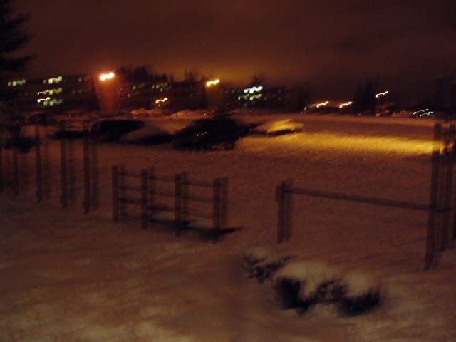 Snow-covered vehicles parked at night with streetlights in the background