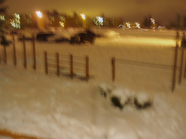 Dark SUV in snowy lot at night with fence and lights