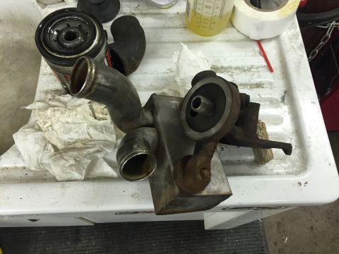 1988 Ford Bronco - A used oil filter and a metal oil cooler assembly with attached hoses are laid out on a white utility sink.