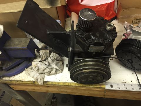 1988 Ford Bronco - A black air conditioning compressor with a K&N air filter sits on a workbench next to a pulley system. A blue vice and some rags are visibl…