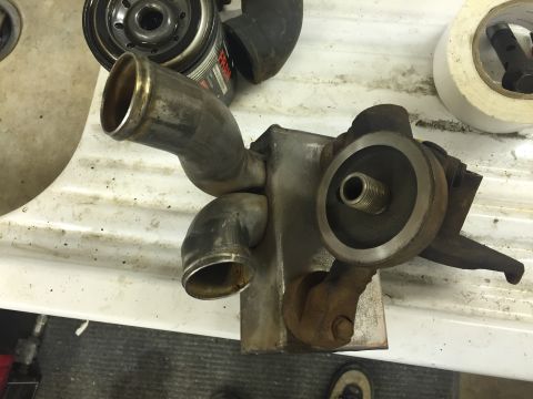 1988 Ford Bronco - A close-up view of a rusty oil cooler assembly with two metal pipes attached. A roll of white tape and a Fram oil filter are visible in the…
