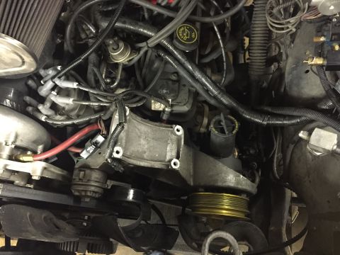 1988 Ford Bronco - Close-up overhead view of a complex engine bay with numerous wires, hoses, and pulleys visible. A gold-colored pulley is prominent in the l…