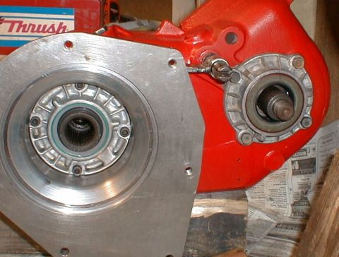 1990 Ford Bronco - Close-up of a red transfer case part with a metal flange and splined shaft, likely for a vehicle.