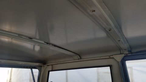 1973 Ford Bronco - The interior ceiling of a vehicle shows a light gray headliner with visible metal support beams and some signs of wear and tear along the s…