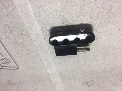 1982 Ford Bronco - A black metal part with three circular openings and a threaded bolt is attached to a textured, light-colored surface. The part is secured w…