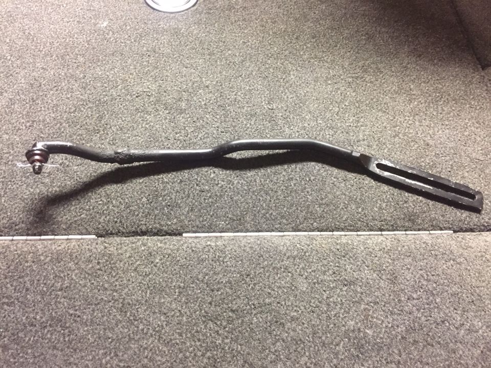 Black tie rod end with ball joint and slotted metal rod on grey carpet.