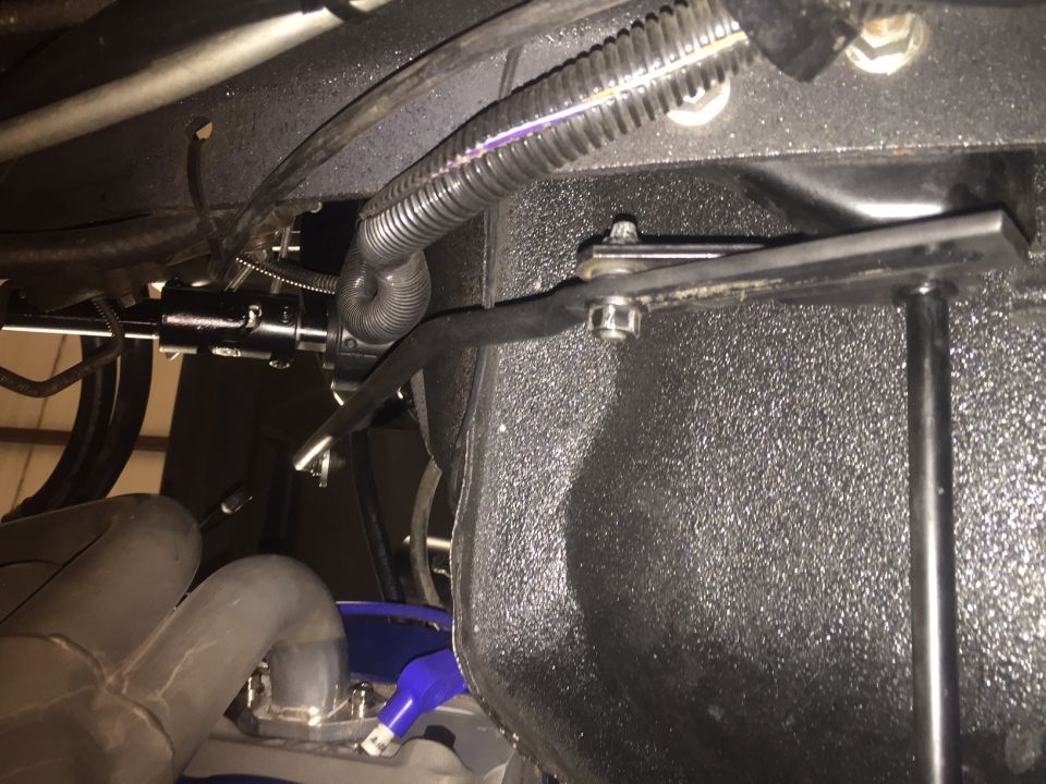 Underside of a vehicle showing steering linkage, corrugated hose, and exhaust pipes.
