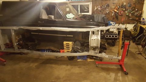 1994 Ford Bronco - A black 1994 Ford Bronco is partially disassembled, with its body lifted off the frame. The engine is mounted on an engine stand, and vario…