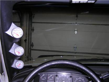 1993 Ford Bronco - Three gauges are mounted on the A-pillar inside a vehicle, with a steering wheel and dashboard visible.