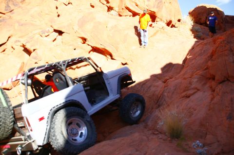 1979 Ford Bronco - A white Ford Bronco is navigating a steep, rocky, off-road trail. Two men are visible in the background, observing the vehicle's progress.