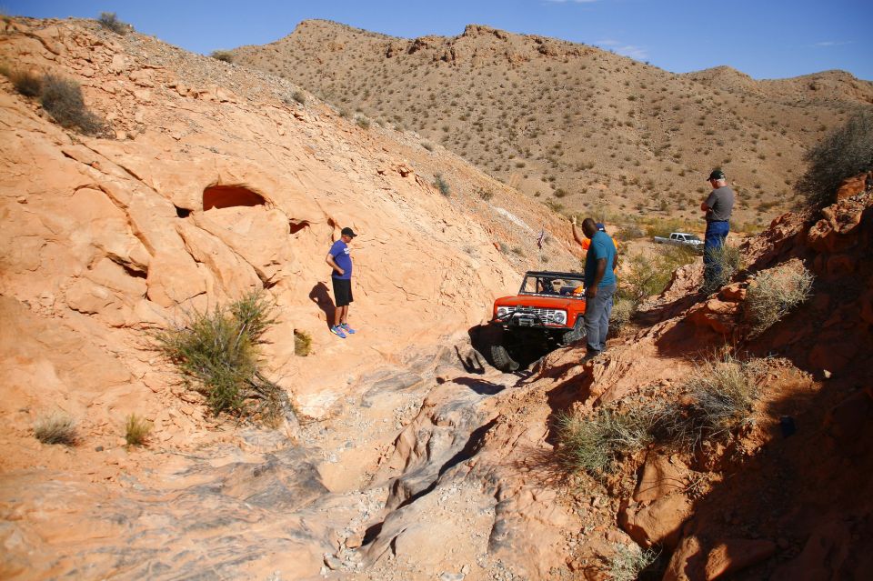 Orange Ford Bronco on a rocky off-road trail with three people.