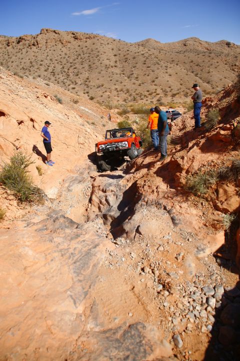 1979 Ford Bronco - An orange Ford Bronco is navigating a steep, rocky off-road trail with several people watching. The vehicle is angled down into a ravine wi…