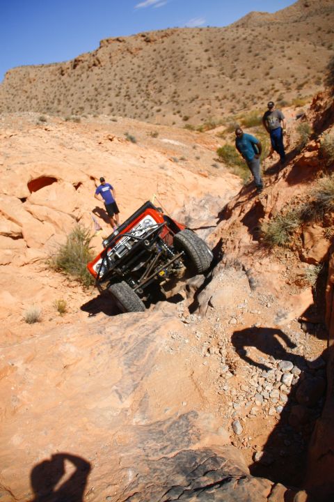 1979 Ford Bronco - A custom red off-road Bronco is navigating a steep, rocky incline with its front wheels elevated. Several people are observing the vehicle…