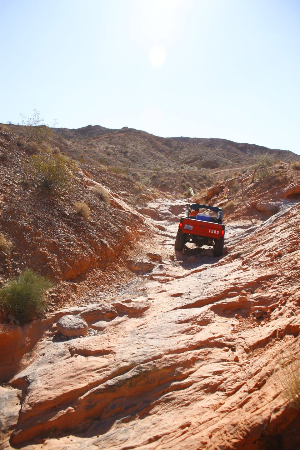 Orange Ford Bronco driving up a rocky desert trail.