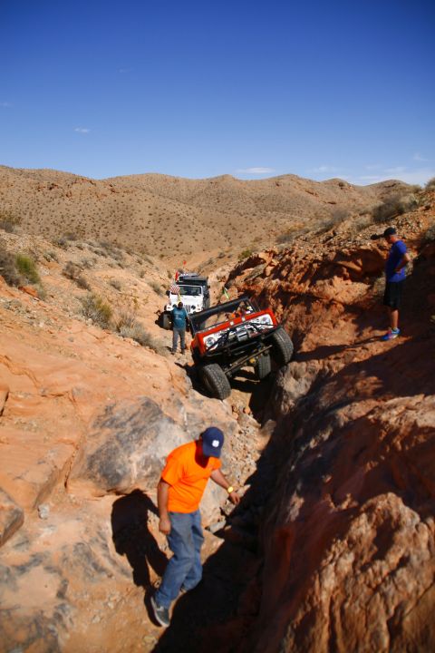 1979 Ford Bronco - An orange 1979 Ford Bronco is navigating a steep, rocky off-road trail, with two other vehicles visible behind it. A person in an orange sh…