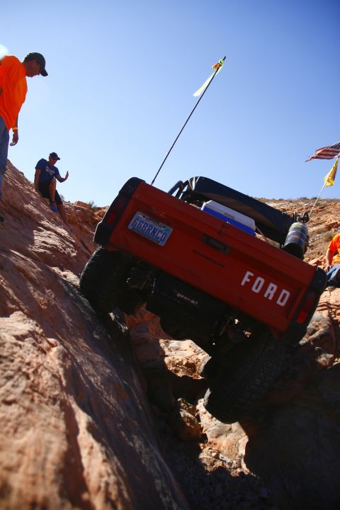 1979 Ford Bronco - A red 1979 Ford Bronco is shown from a low angle, climbing a steep, rocky incline under a clear blue sky. The license plate reads "66BRNCO"…
