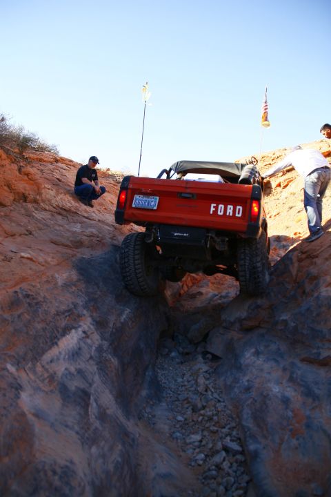 1979 Ford Bronco - An orange Ford Bronco is navigating a steep, rocky off-road trail. Two people are visible near the vehicle, one watching from the side and…