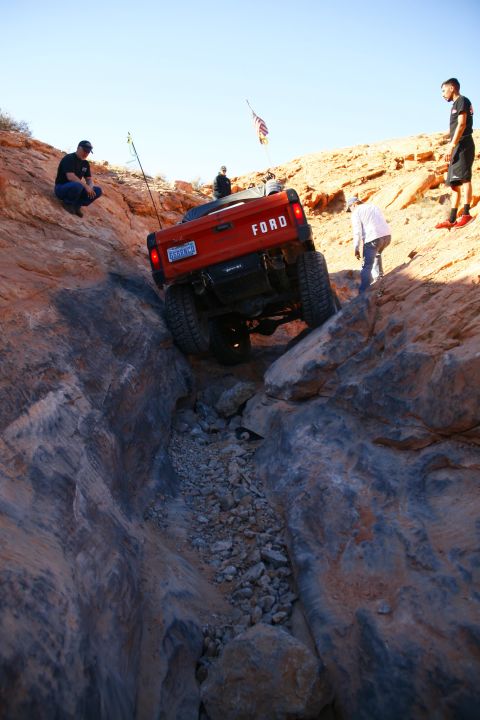 1979 Ford Bronco - An orange Ford pickup truck navigates a narrow, rocky canyon with several people observing. The truck is angled downwards into the canyon,…