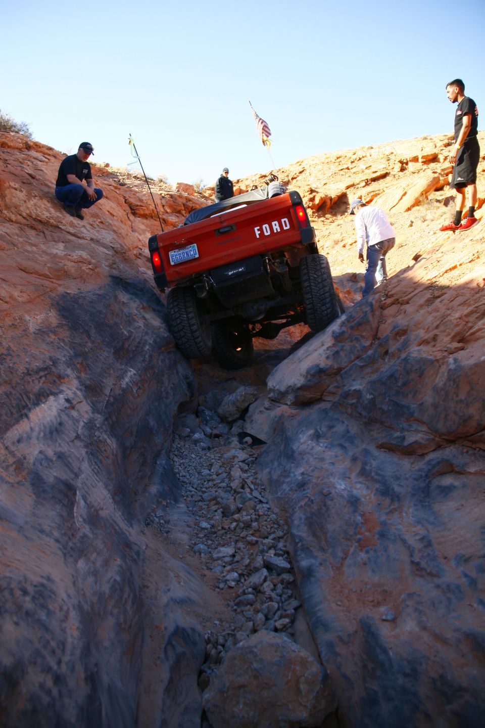 Orange Ford pickup truck driving down a rocky canyon with people watching.