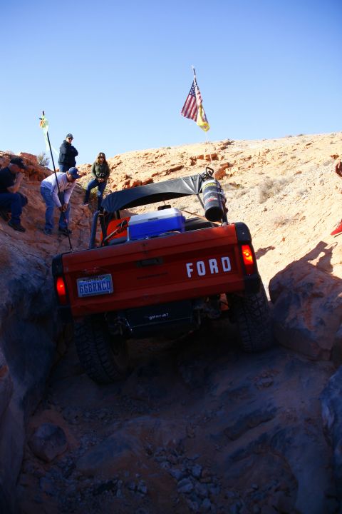 1979 Ford Bronco - A bright orange 1979 Ford Bronco is navigating a rocky, off-road trail. The rear of the vehicle is visible, showing the license plate, tail…
