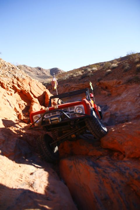 1979 Ford Bronco - A red 1979 Ford Bronco is navigating a steep, rocky off-road trail with its front tires angled towards the top of the incline. The vehicle…