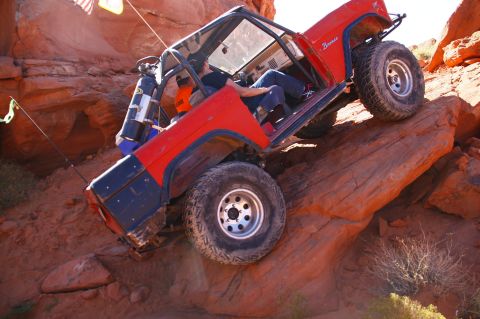 1979 Ford Bronco - A red Ford Bronco is navigating a steep, rocky incline in a desert environment. The vehicle is tilted at a sharp angle, with its tires grip…