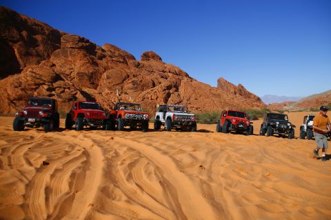 1979 Ford Bronco - A line of off-road vehicles, including a white Ford Bronco, are parked on a sandy desert dune with red rock formations in the background un…