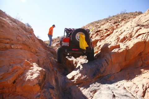 1979 Ford Bronco - A modified red and silver Ford Bronco navigates a rocky, off-road trail. A person in an orange shirt stands on the side of the trail, obser…