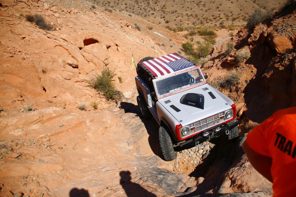 White Ford Bronco with American flag roof decal on a rocky off-road trail.