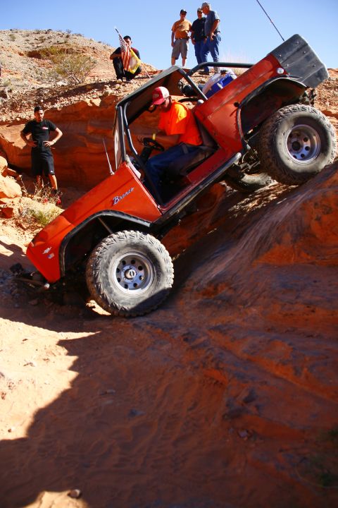 1979 Ford Bronco - An orange 1979 Ford Bronco is navigating a steep, rocky incline off-road. The vehicle is tilted at a sharp angle, with its front tires grip…