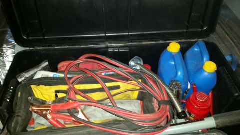 1979 Ford Bronco - An open black storage box filled with various automotive emergency items including jumper cables, two blue plastic fuel containers with yel…