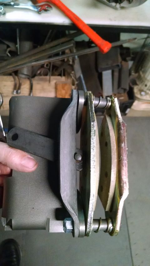 1985 Jeep CJ7 - A close-up view shows a person's hand holding a brake caliper assembly with new brake pads installed. The assembly is attached to a dark gr…