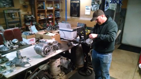 1985 Jeep CJ7 - A man in a garage is working on a large metal automotive part, possibly a transmission or transfer case, laid out on a workbench next to va…