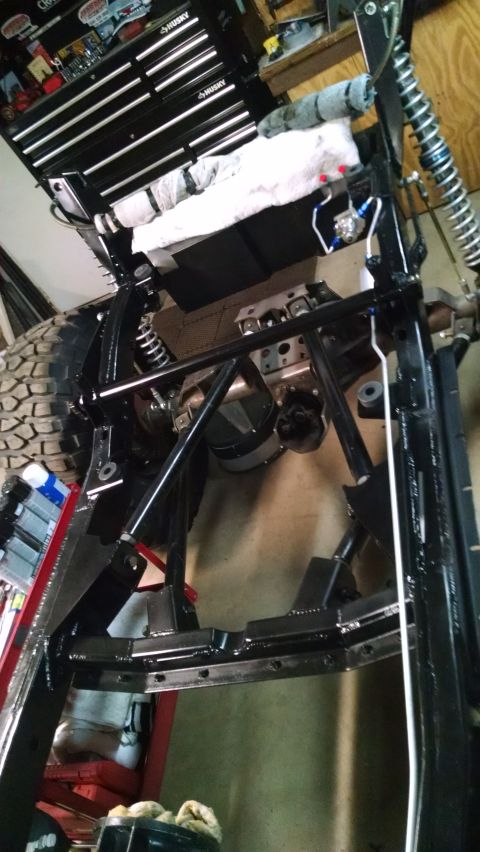 1985 Jeep CJ7 - The underside of a vehicle frame is shown, with various suspension components and a large tire visible. A black Husky tool chest is in the…