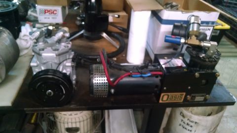 1985 Jeep CJ7 - Two automotive air conditioning compressors are shown on a workbench. One is silver and has a black clutch, while the other is black and ha…