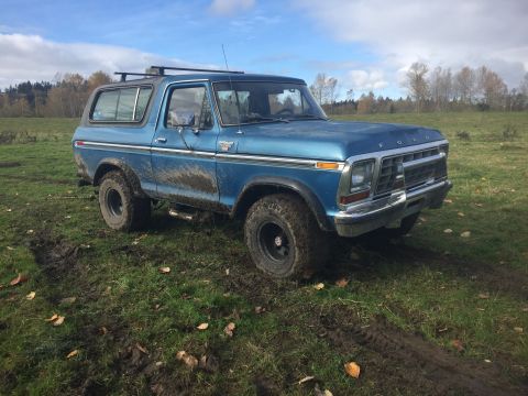 1979 Ford Bronco - This blue 1979 Ford Bronco is shown off-road in a grassy, muddy area under a partly cloudy sky.